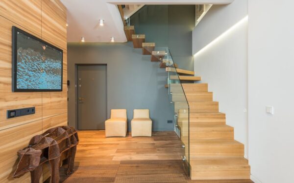 Contemporary stylish house hallway interior with creative statue under TV set cozy chairs and wooden stairway