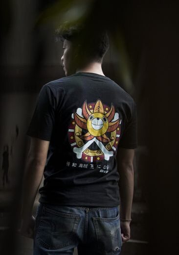 Man wearing black t-shirt with colorful graphic design and jeans in a natural setting.